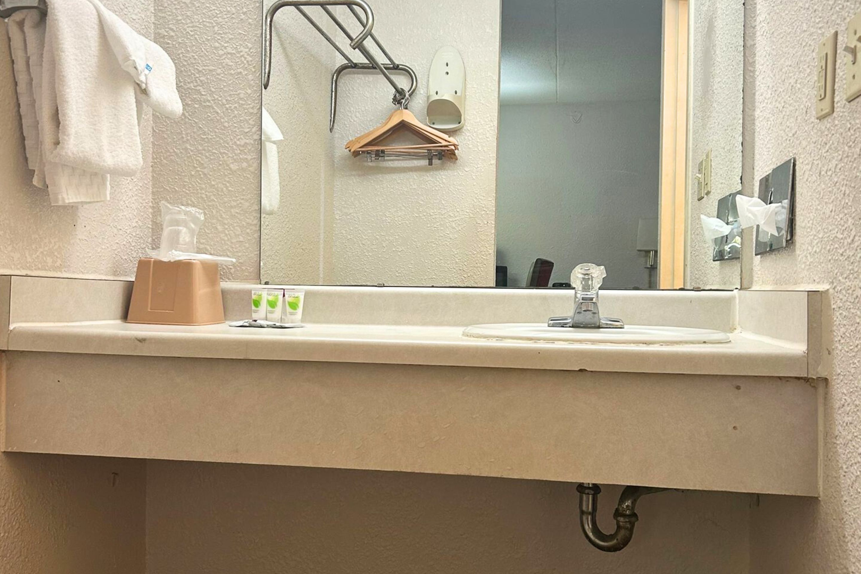 A bathroom with a sink, mirror, towel rack, and a hanging shoe rack.