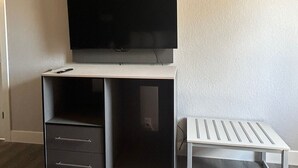 A modern room with a flat-screen TV mounted on a white desk, a small white table, and a black cabinet with drawers. - Key Inn Roseville (Roseville)