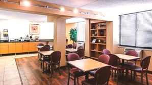 A dining area with wooden flooring, tables, and chairs. There is a kitchen area with cabinets and appliances. A plant is visible in the background. - Key Inn Roseville (Roseville)