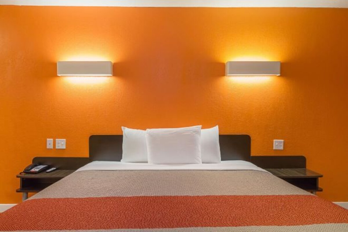 A hotel room with an orange wall, a bed with white bedding, and two wall-mounted light fixtures.