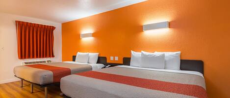 A hotel room with two beds, orange walls, and a wooden floor.