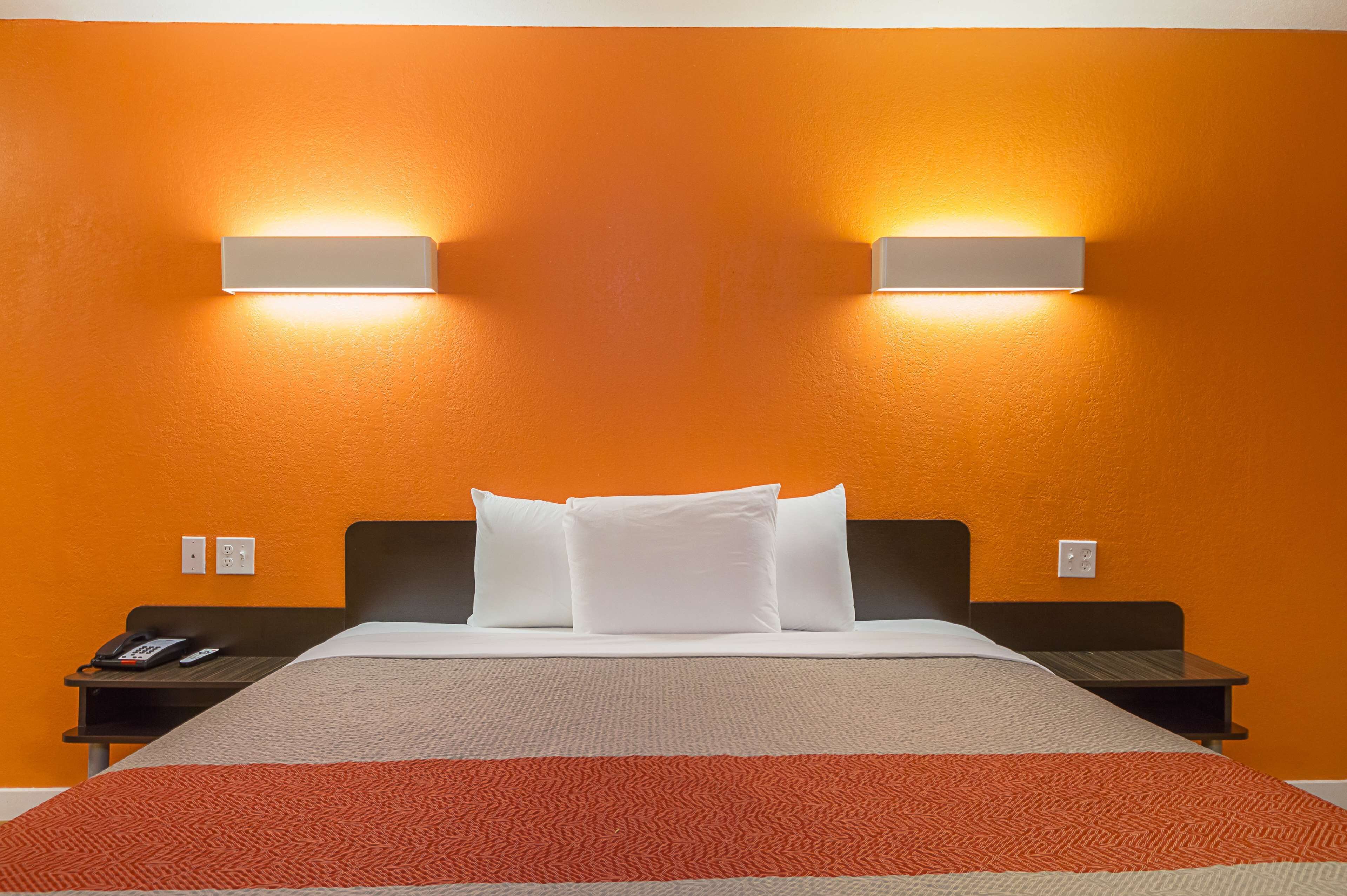 A hotel room with an orange wall, a bed with white bedding, two bedside tables, and a red and beige blanket.