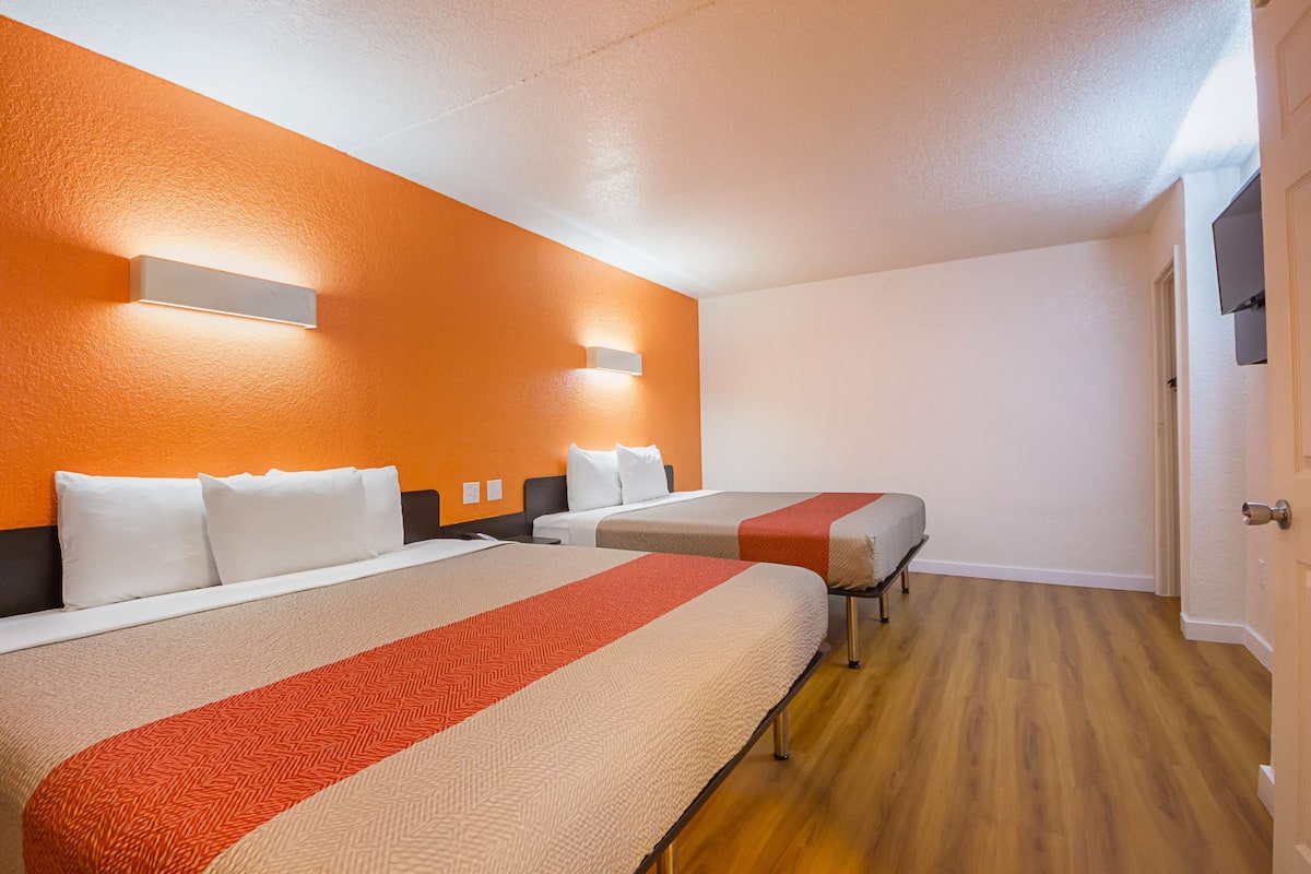 Une chambre d’hôtel avec deux lits, un plancher en bois et des murs orange.