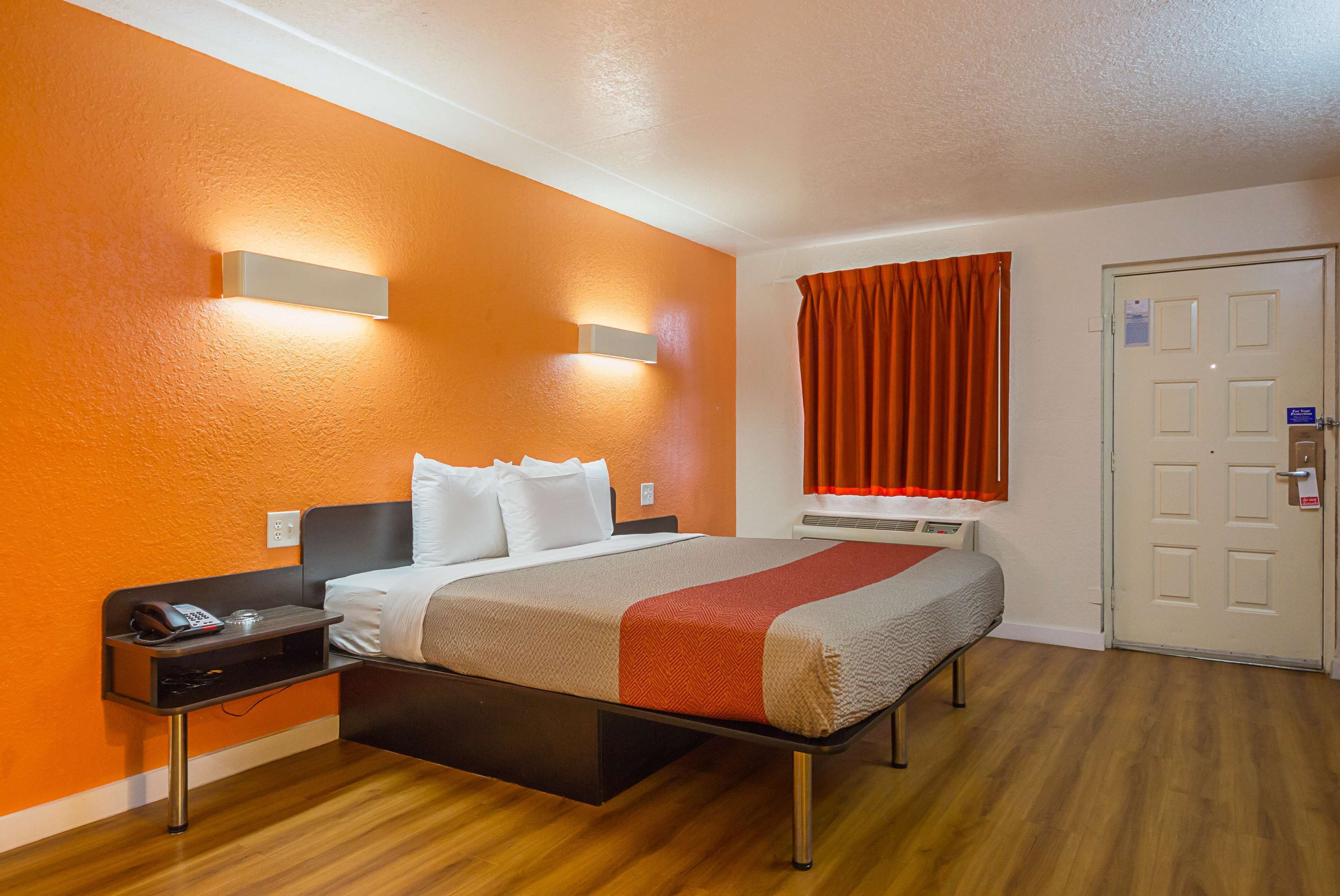 A hotel room with a bed, bedside table, and a window with curtains.