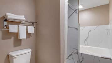 A bathroom with a toilet, a towel rack with towels, and a shower area with a marble wall.
