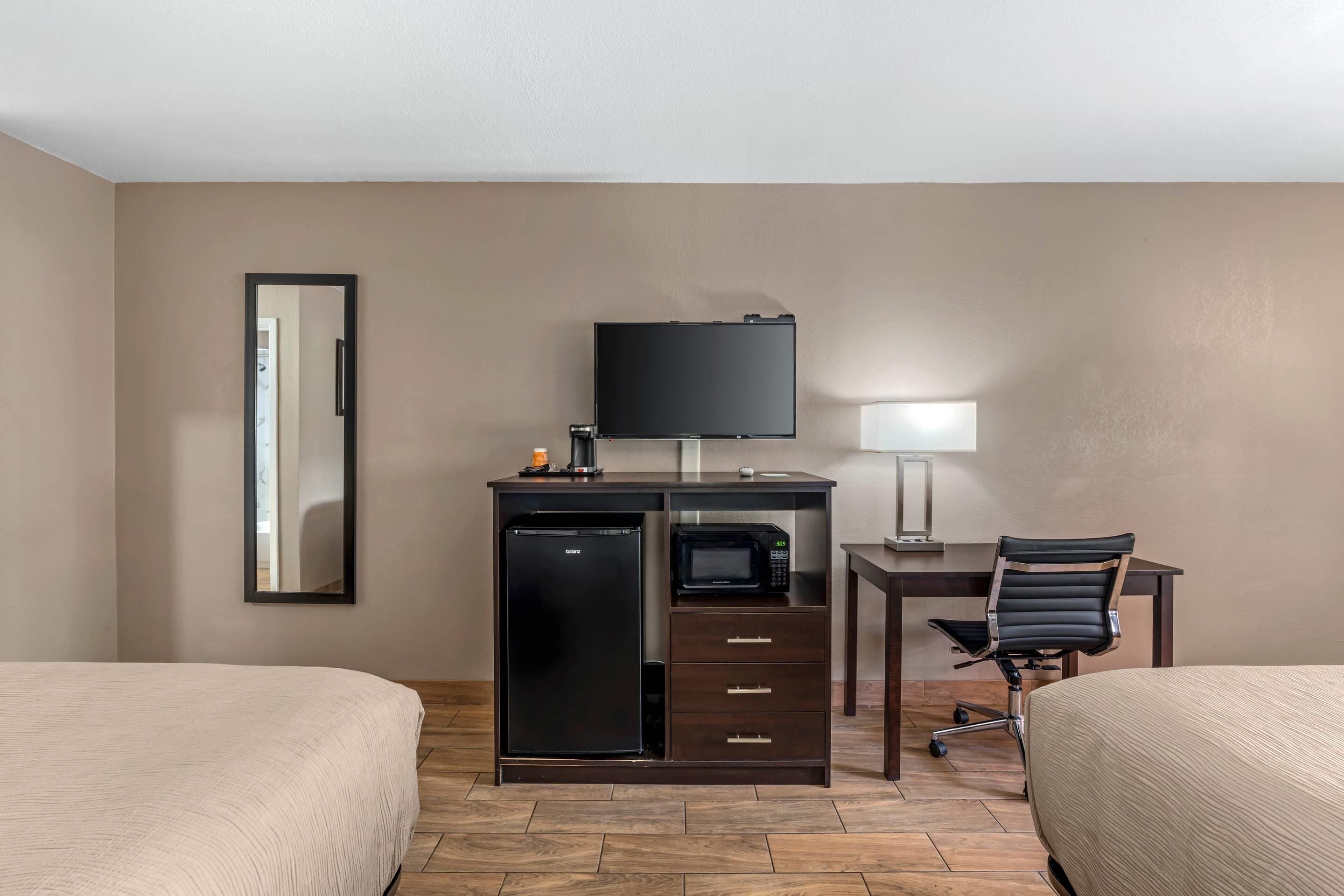 Une chambre d’hôtel avec deux lits, un bureau avec une télévision, un réfrigérateur, un four à micro-ondes et une chaise.