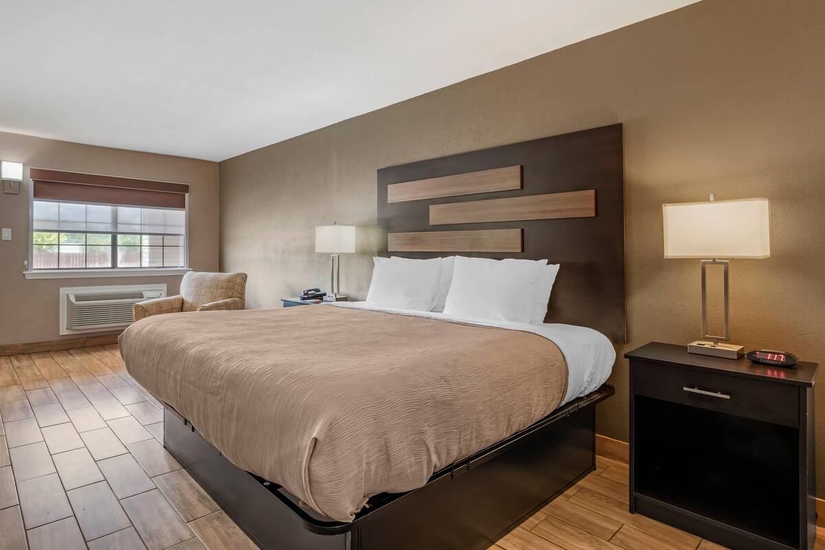 A hotel room with a large bed, bedside lamps, a nightstand, and a window with blinds.