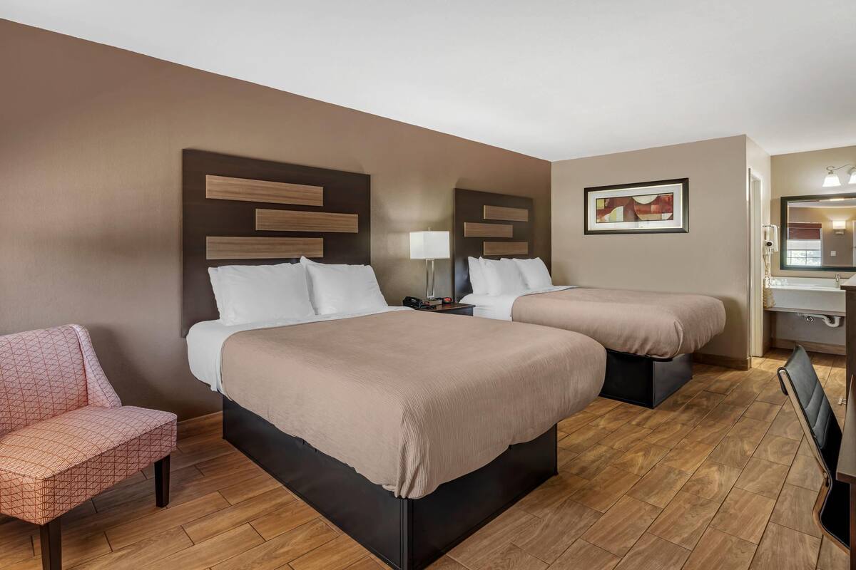 A hotel room with two beds, a chair, a desk, and a mirror.