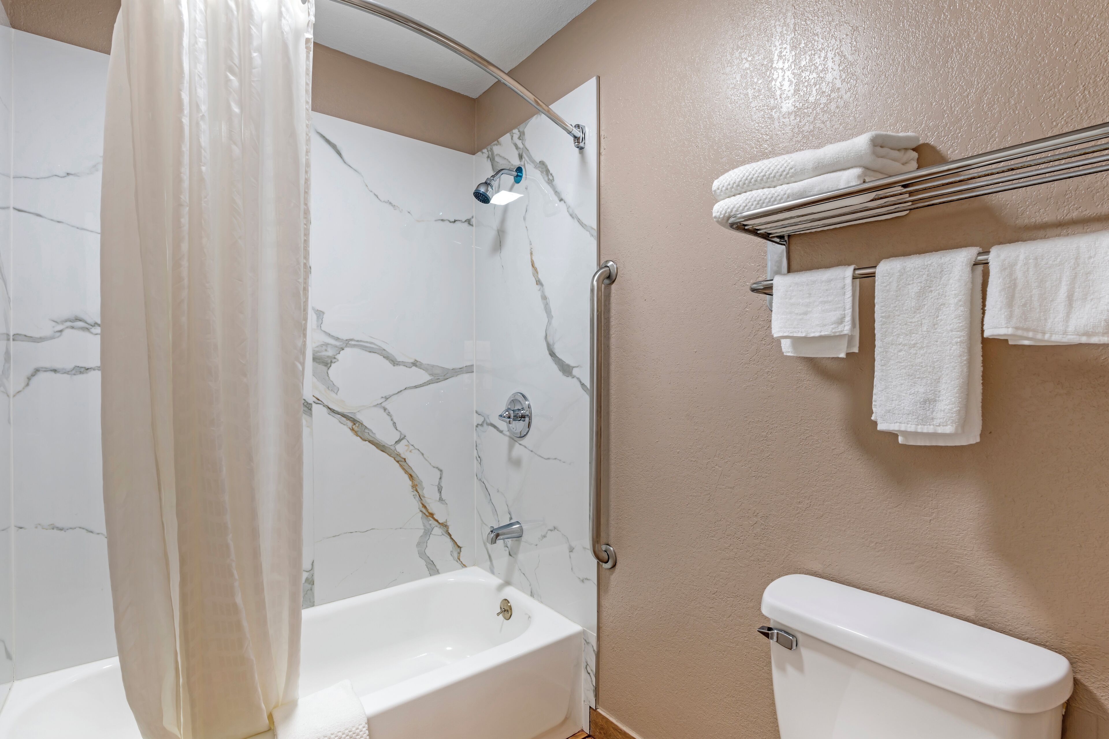 A bathroom with a shower, a bathtub, a toilet, and a towel rack with towels.