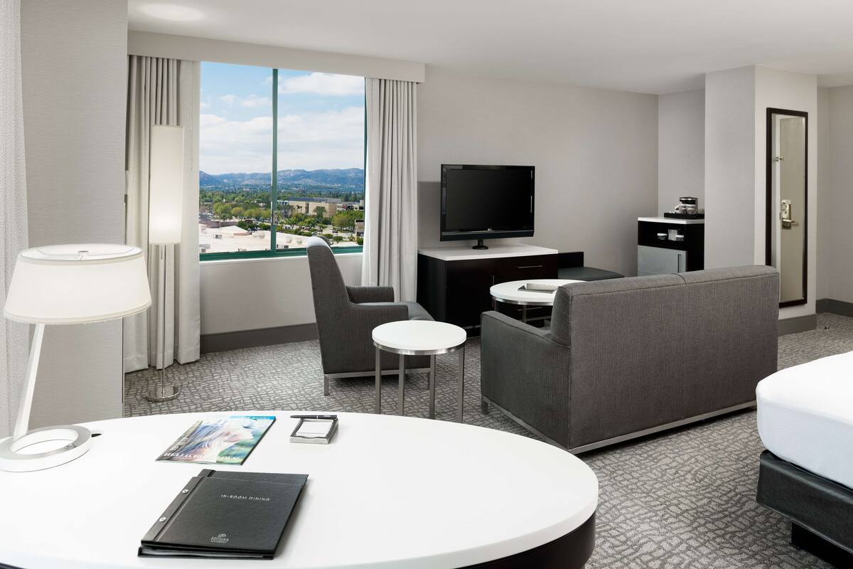 Una habitación de hotel con cama, escritorio, televisión, silla y vistas a la ciudad.