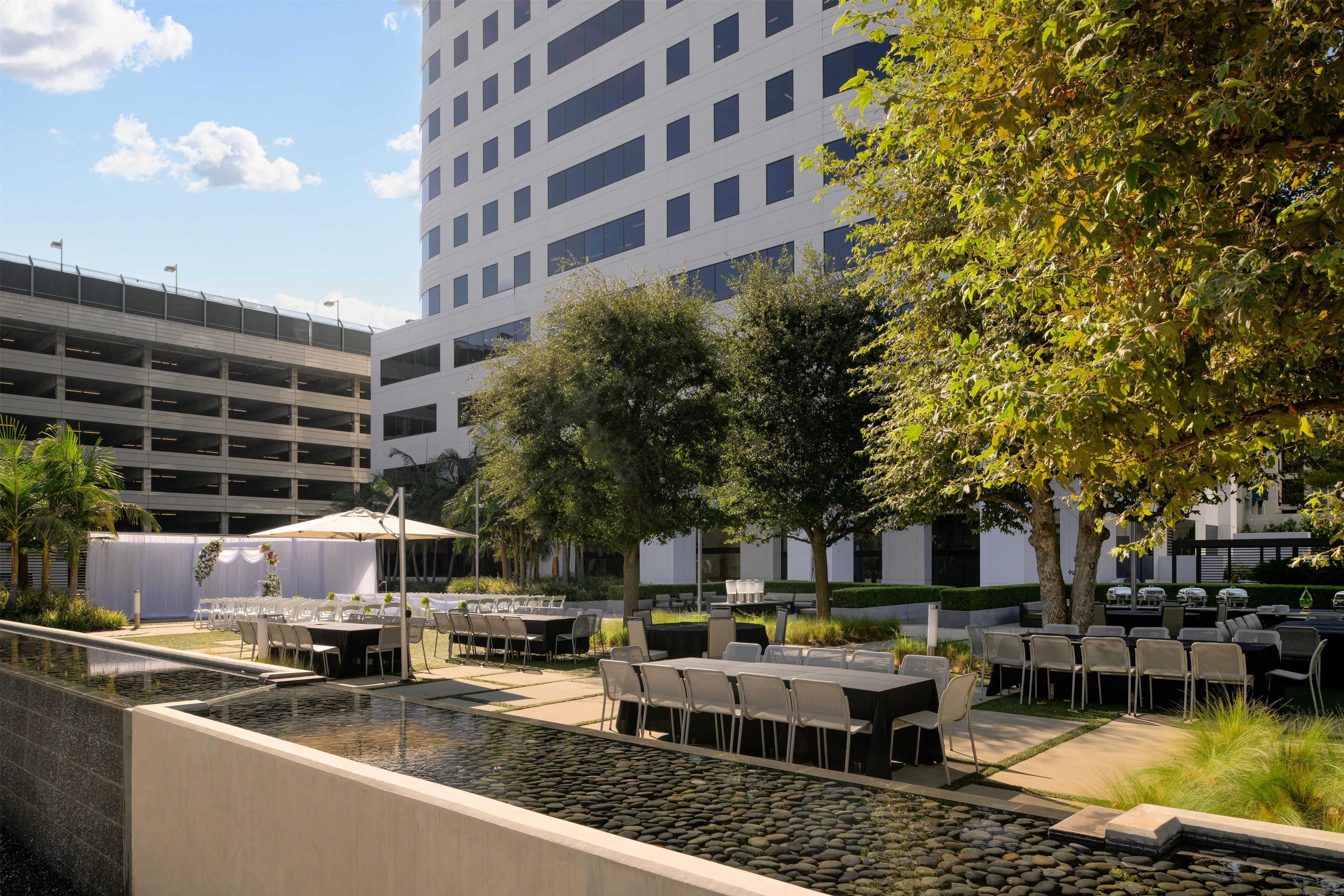 An outdoor dining area with tables and chairs, a pool with rocks, and a building in the background.