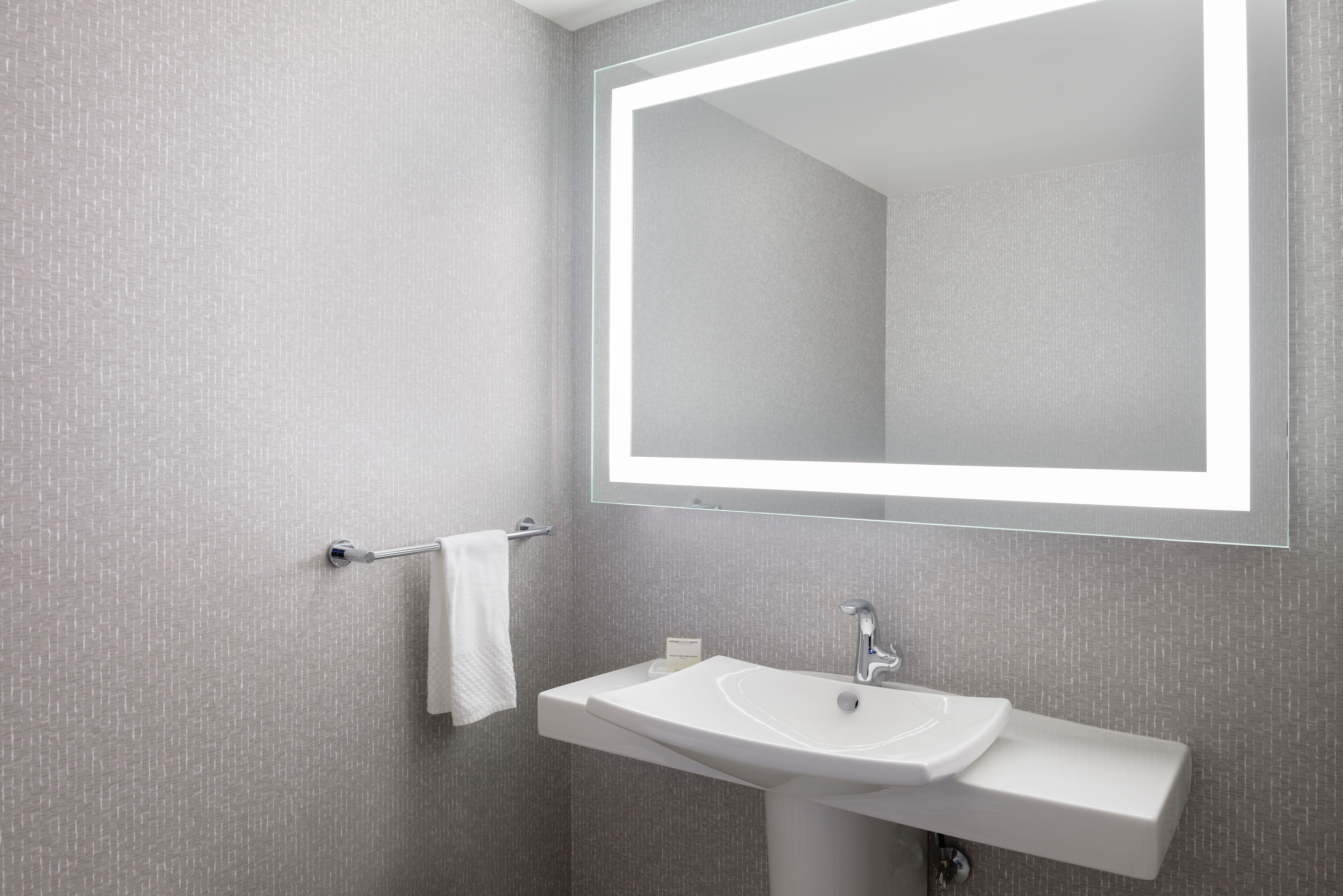 A modern bathroom with a large mirror, a white sink, and a towel rack.