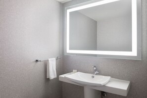 Une salle de bain moderne avec un grand miroir, un lavabo blanc et un porte-serviettes.