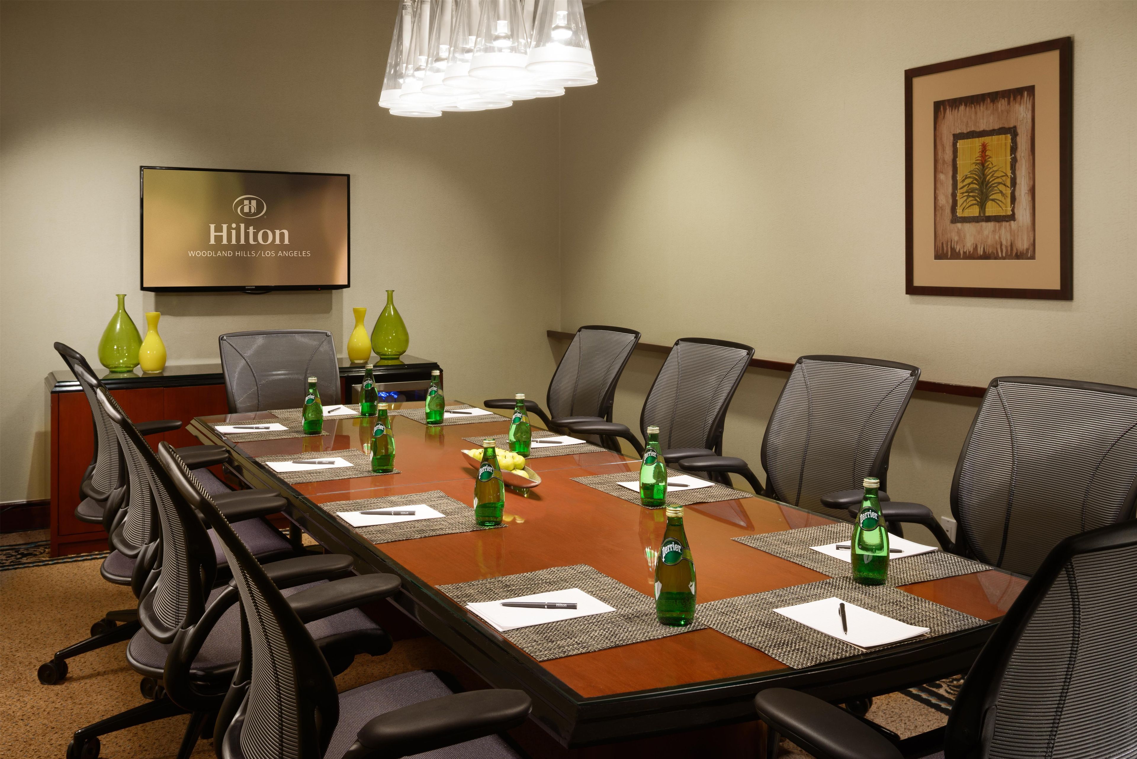 A conference room with a long table, chairs, and a television displaying the Hilton logo.
