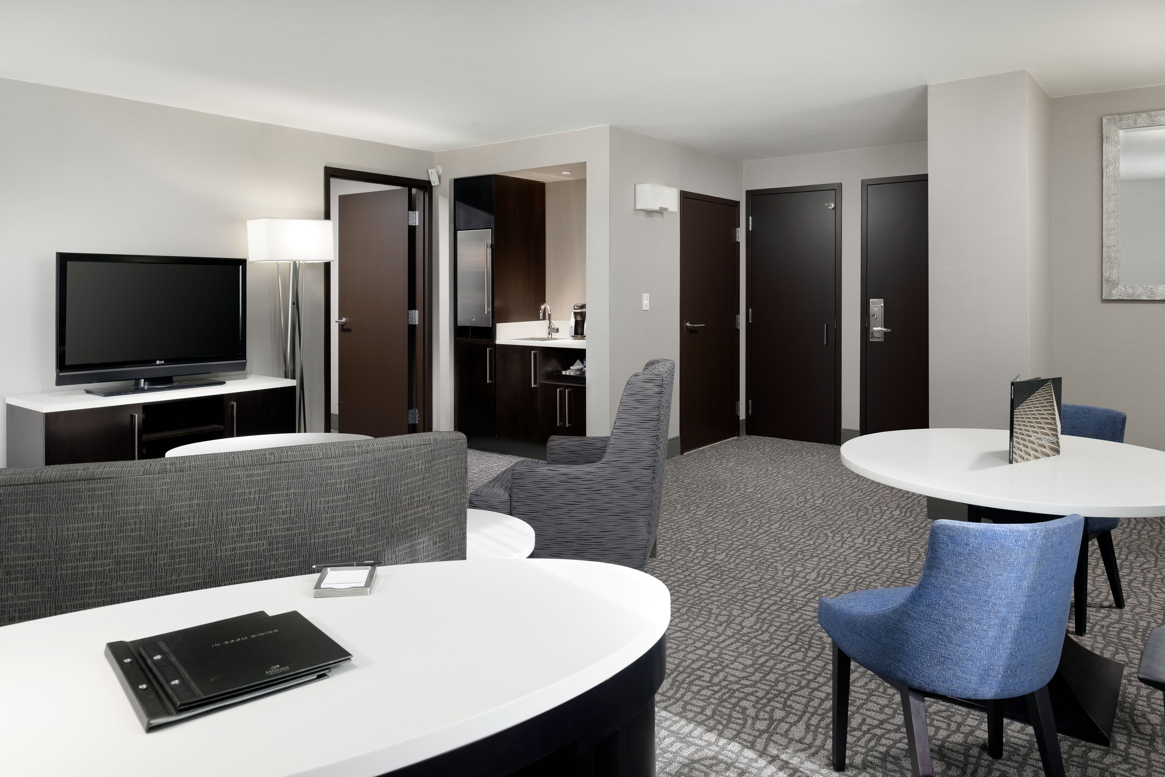 Habitación de hotel con televisor de pantalla plana, sofá, mesa de comedor con sillas, kitchenette y baño.