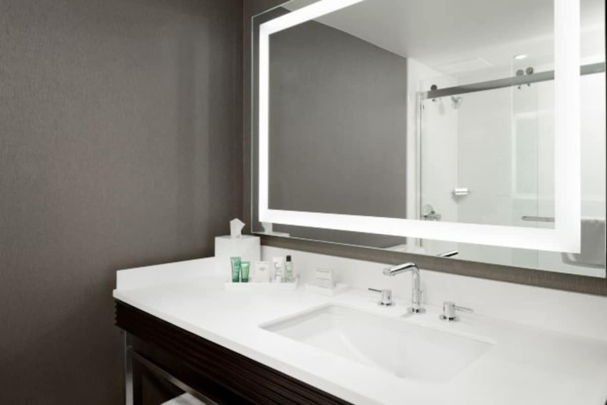 Un baño moderno con un espejo grande, un lavamanos blanco y un mueble bajo lavabo oscuro.