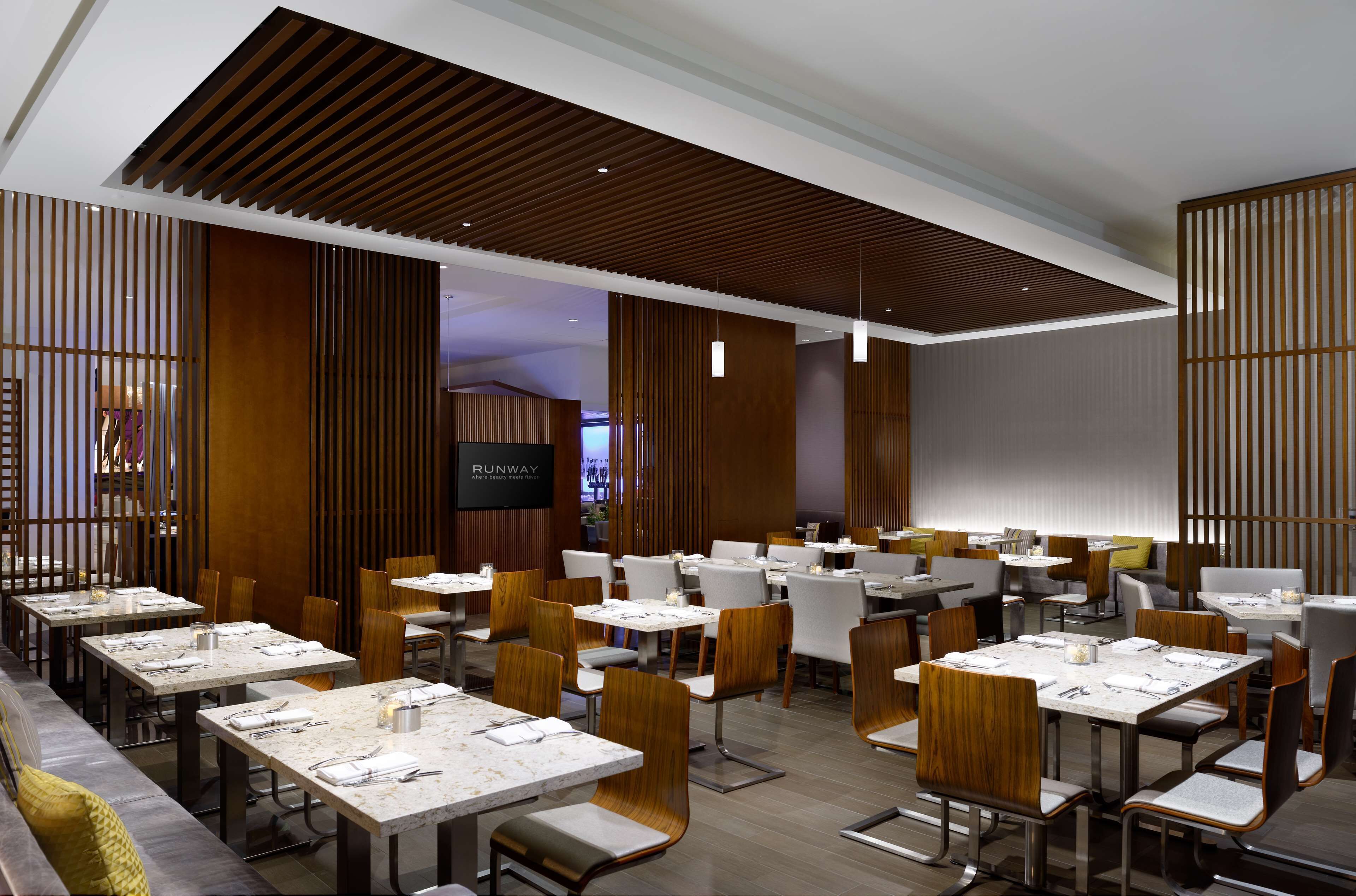 A modern restaurant with multiple dining tables and chairs, wooden paneling on the walls, and pendant lighting.