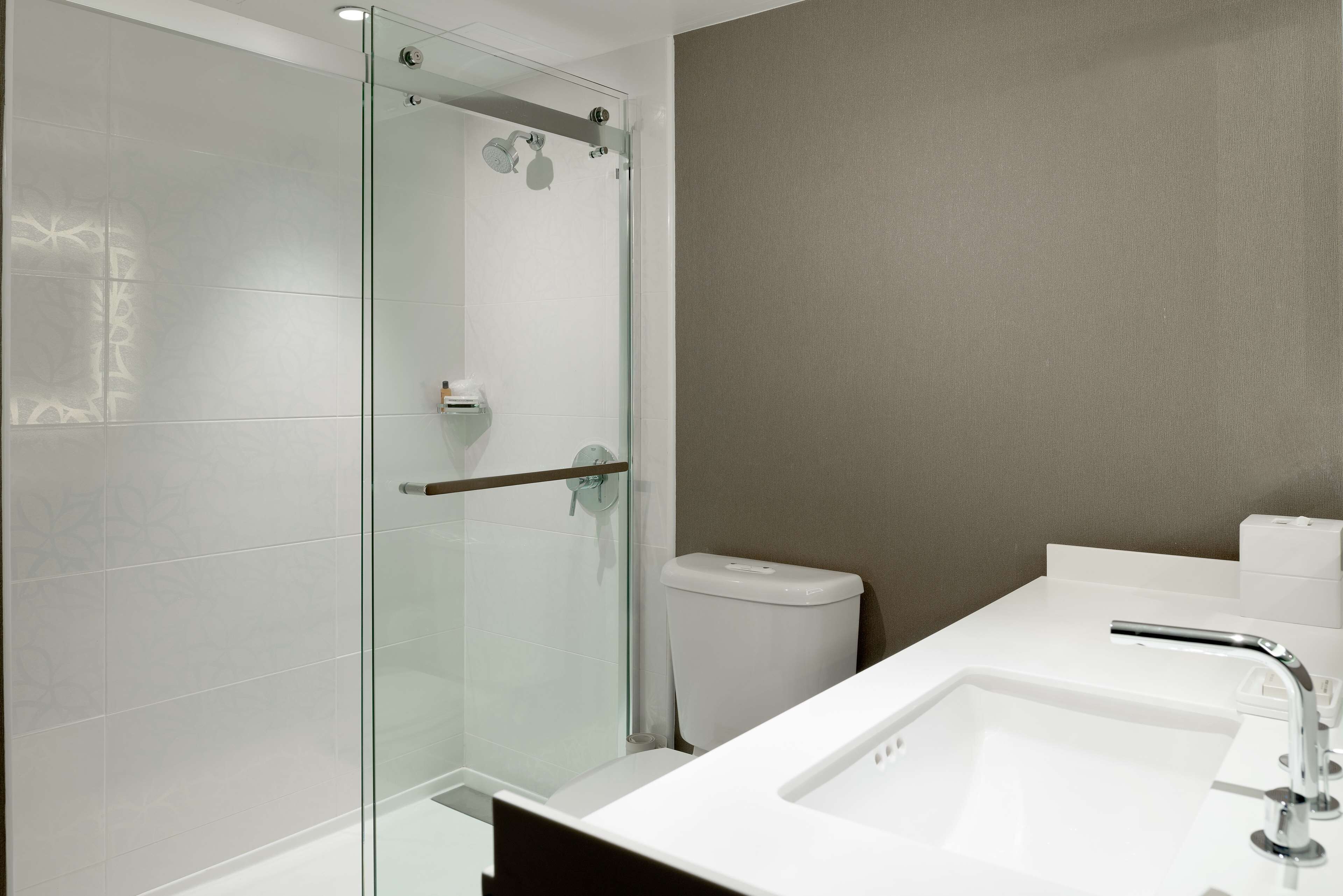 Un baño moderno con cabina de ducha de vidrio, un lavamanos blanco y una pared color beige.