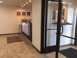 A hotel reception area with a digital screen displaying a message, a reception desk, and a glass door leading inside.