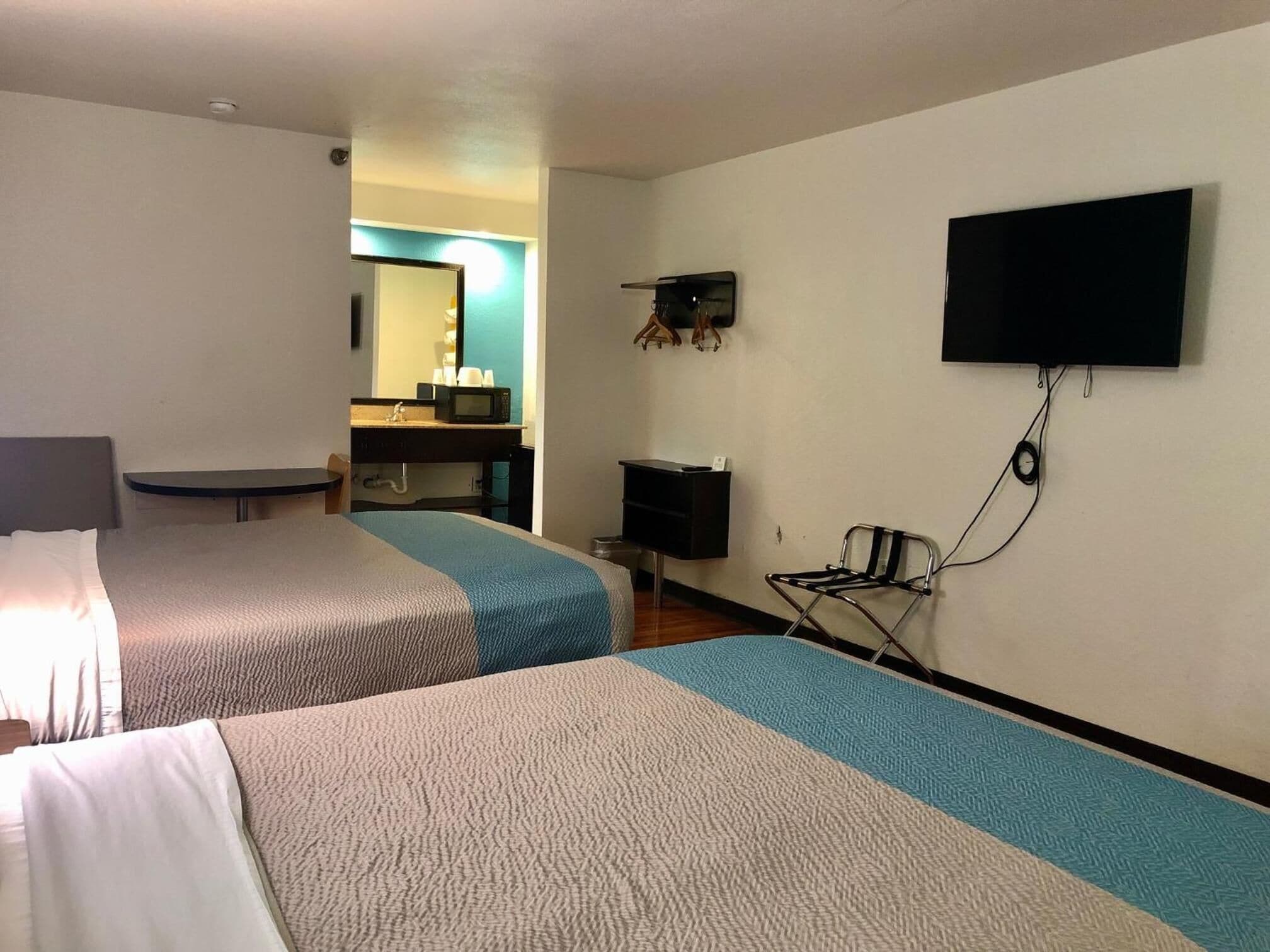 Une chambre d’hôtel avec deux lits, un bureau, une chaise, une télévision et une salle de bain visible au fond.