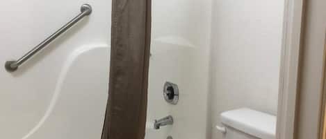 Un baño con ducha, inodoro y barra de apoyo.