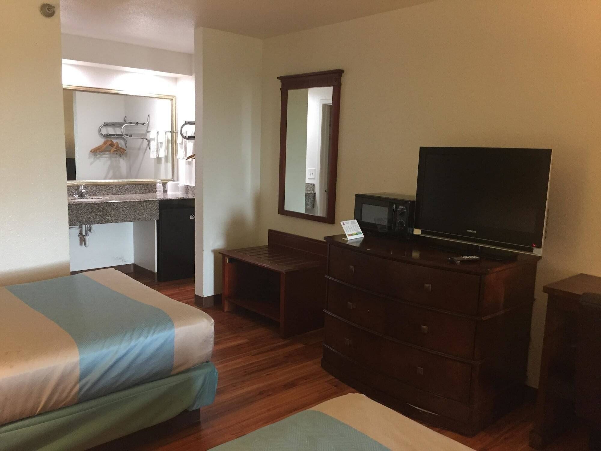 Habitación de hotel con dos camas, televisión, cómoda, espejo y kitchenette con lavabo y armarios.