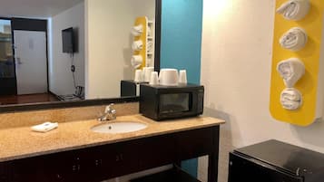 A hotel bathroom with a sink, mirror, towel dispenser, and a microwave.
