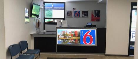 Un espace d’accueil dans un motel, comprenant un comptoir, des chaises et une grande enseigne publicitaire pour le motel.