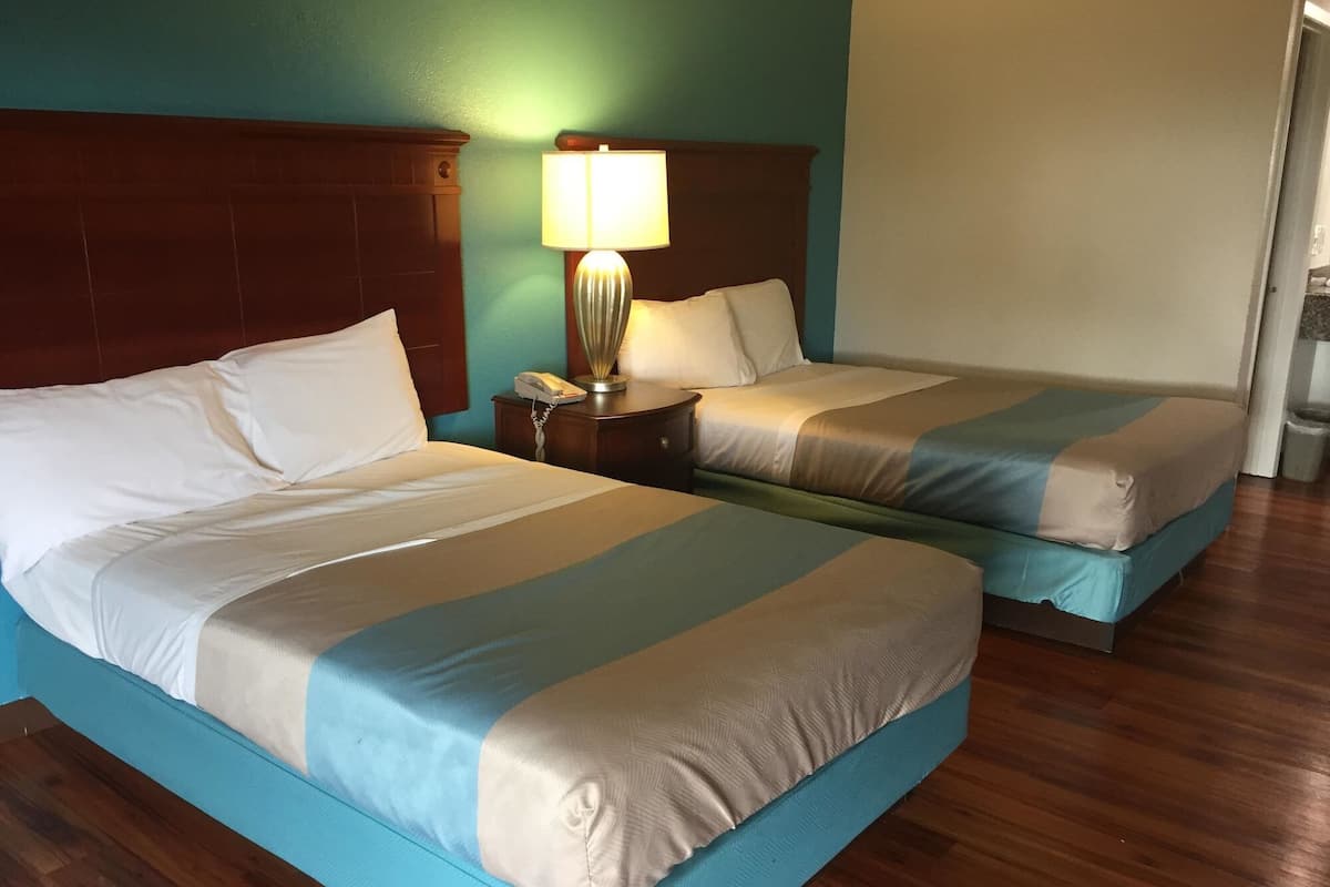 Une chambre d’hôtel avec deux lits, une tête de lit en bois, une lampe de chevet et un téléphone sur la table de chevet.