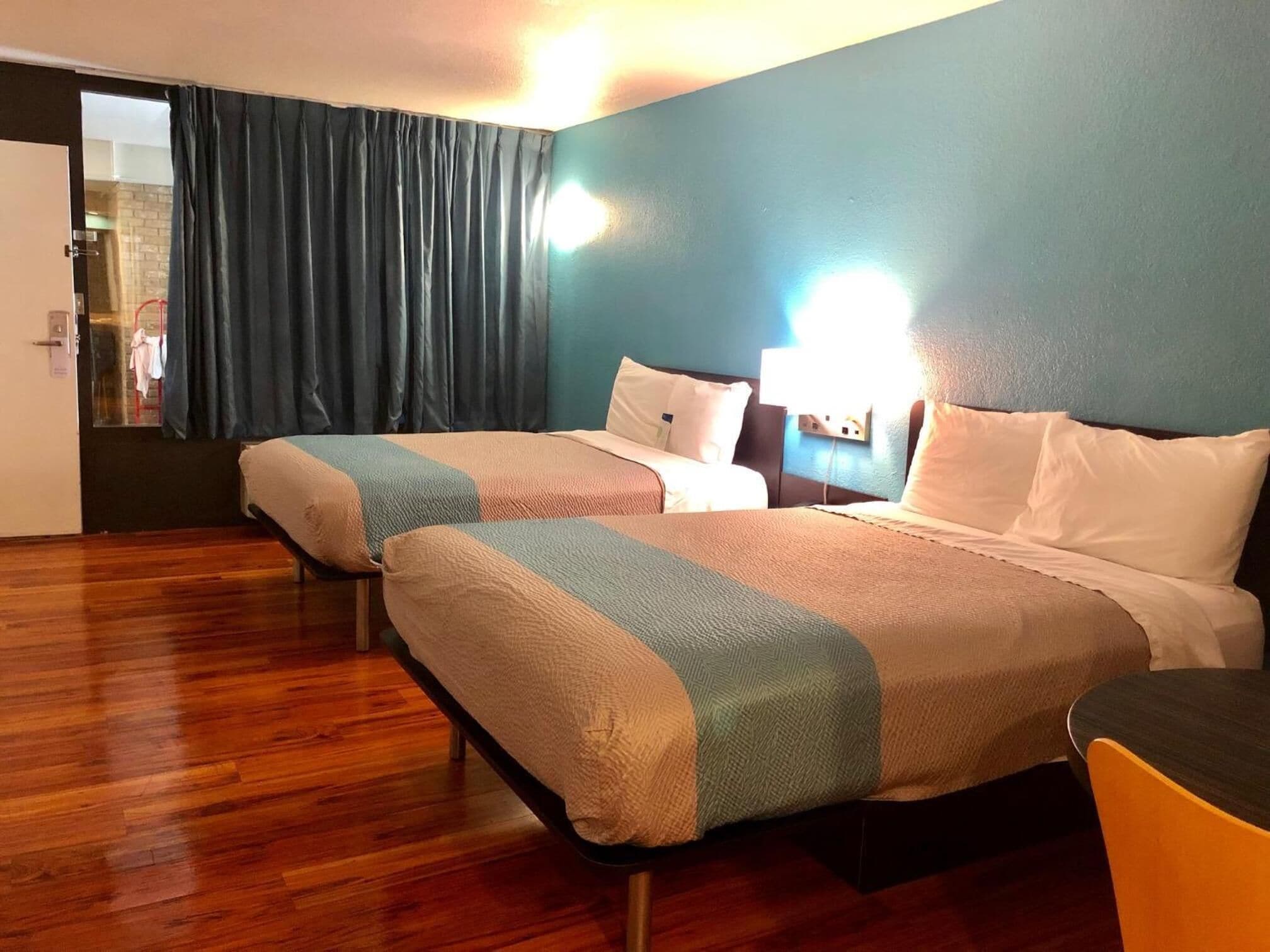 Une chambre d’hôtel avec deux lits, un plancher en bois, un mur bleu et une fenêtre avec des rideaux.