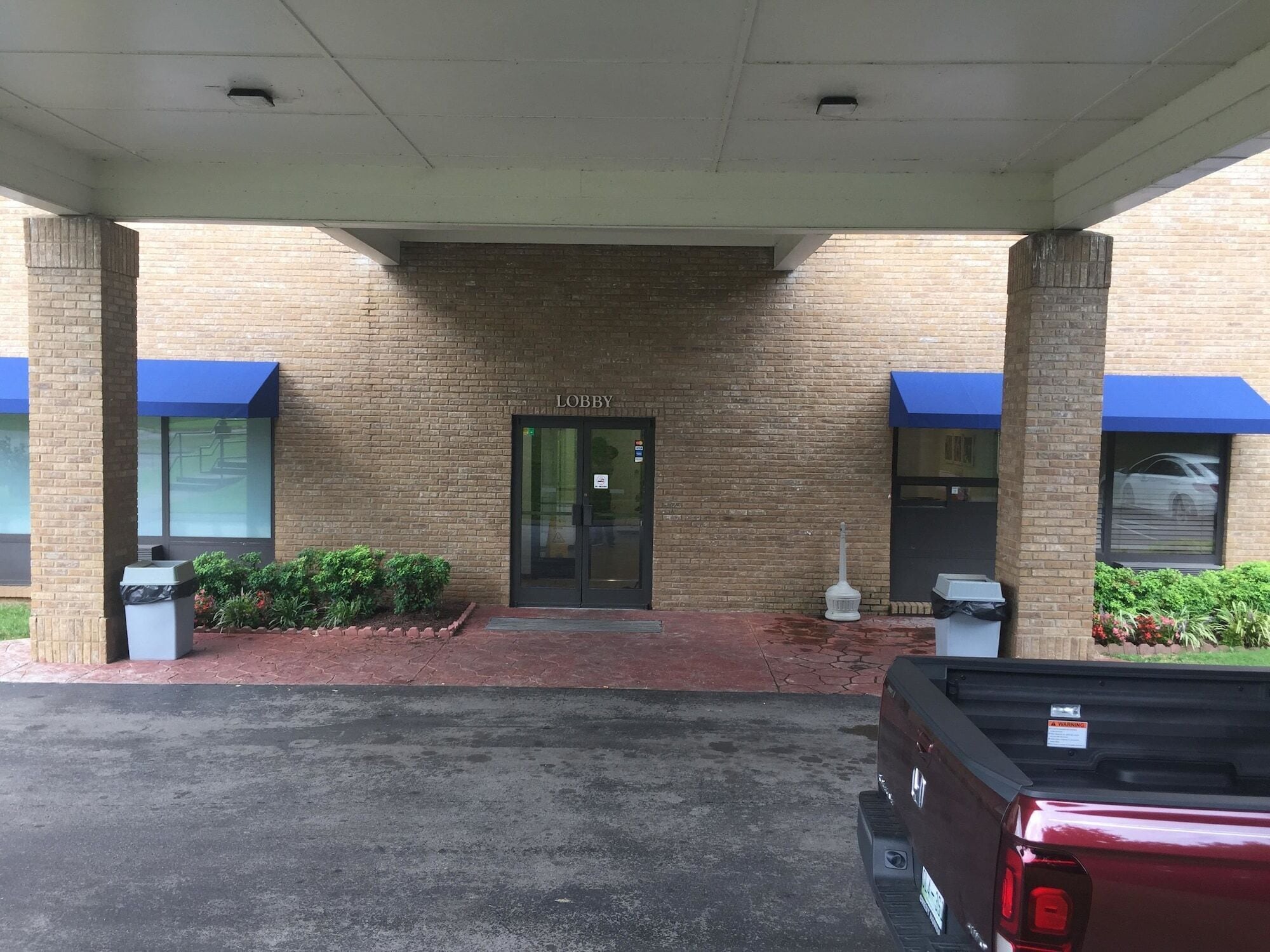 A building entrance with a brick facade, a glass door labeled "Lobby," and a covered parking area.