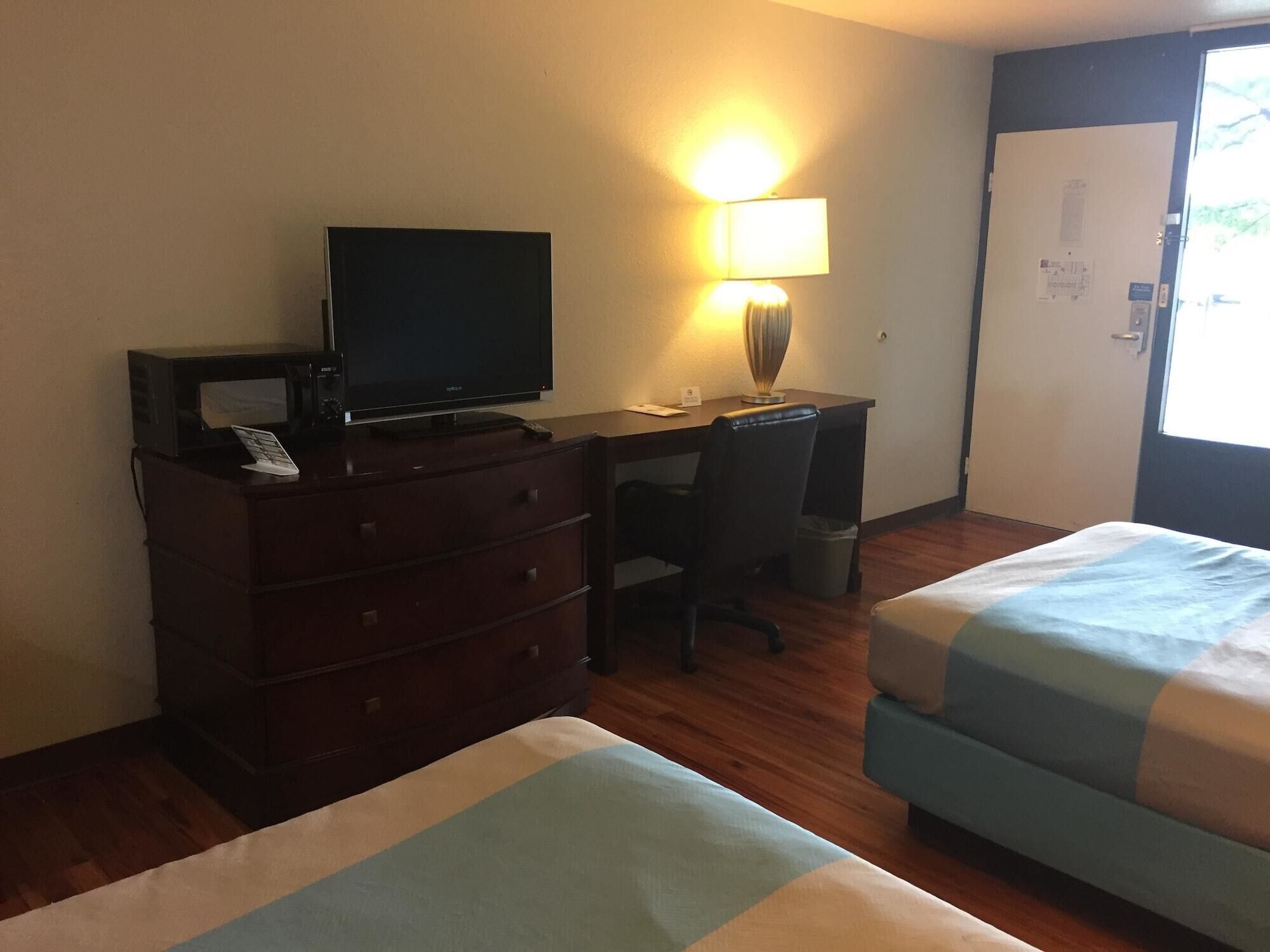 Una habitación de hotel con escritorio, televisión, lámpara, cama y armario.