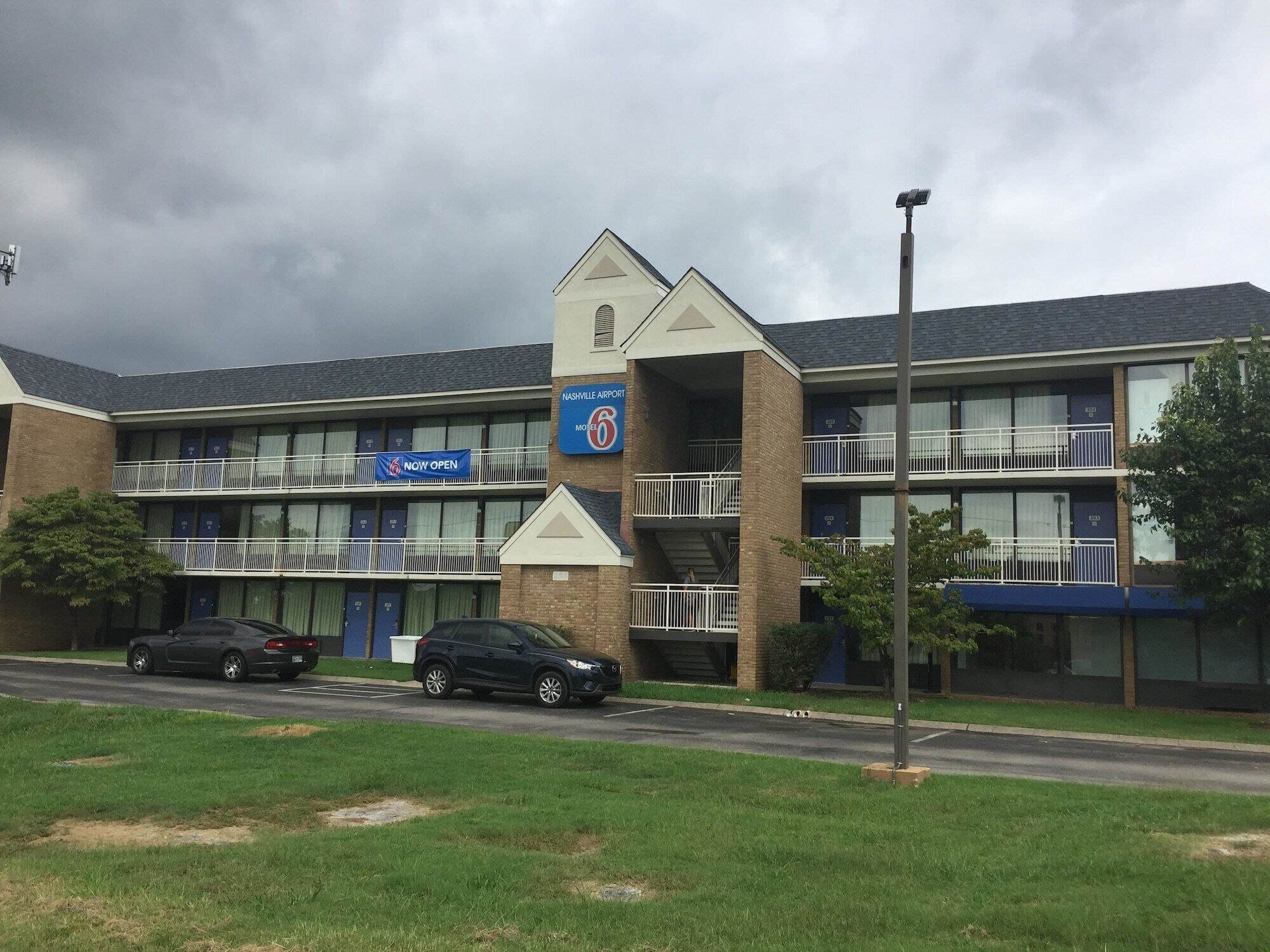 A motel with a 'Now Open' sign, a parking lot, and a building with multiple floors and balconies.