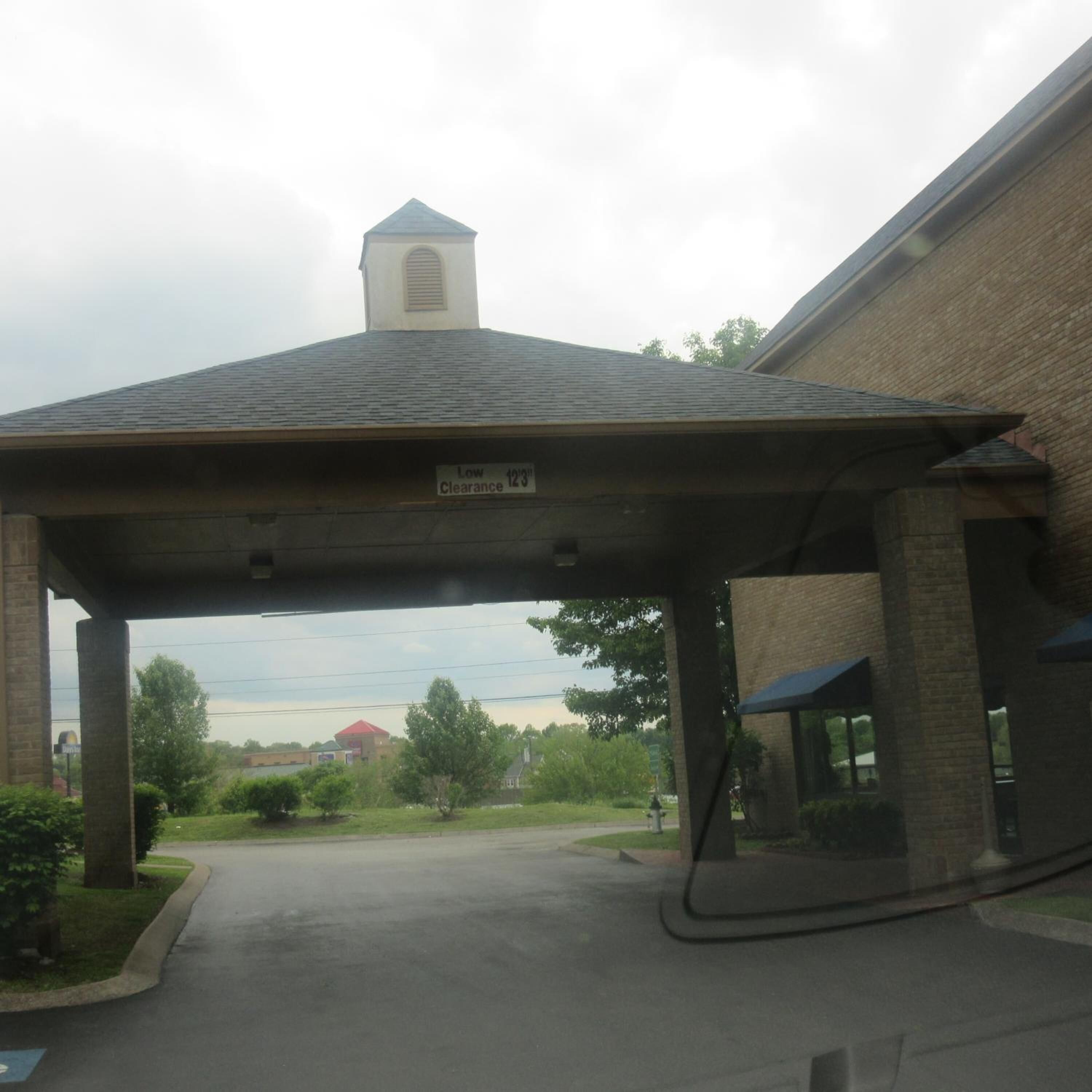 A covered parking area with a low clearance sign, brick building, and a view of the surrounding area.
