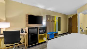 A hotel room with a bed, a desk with a computer, a refrigerator, a microwave, a television, and a wardrobe.