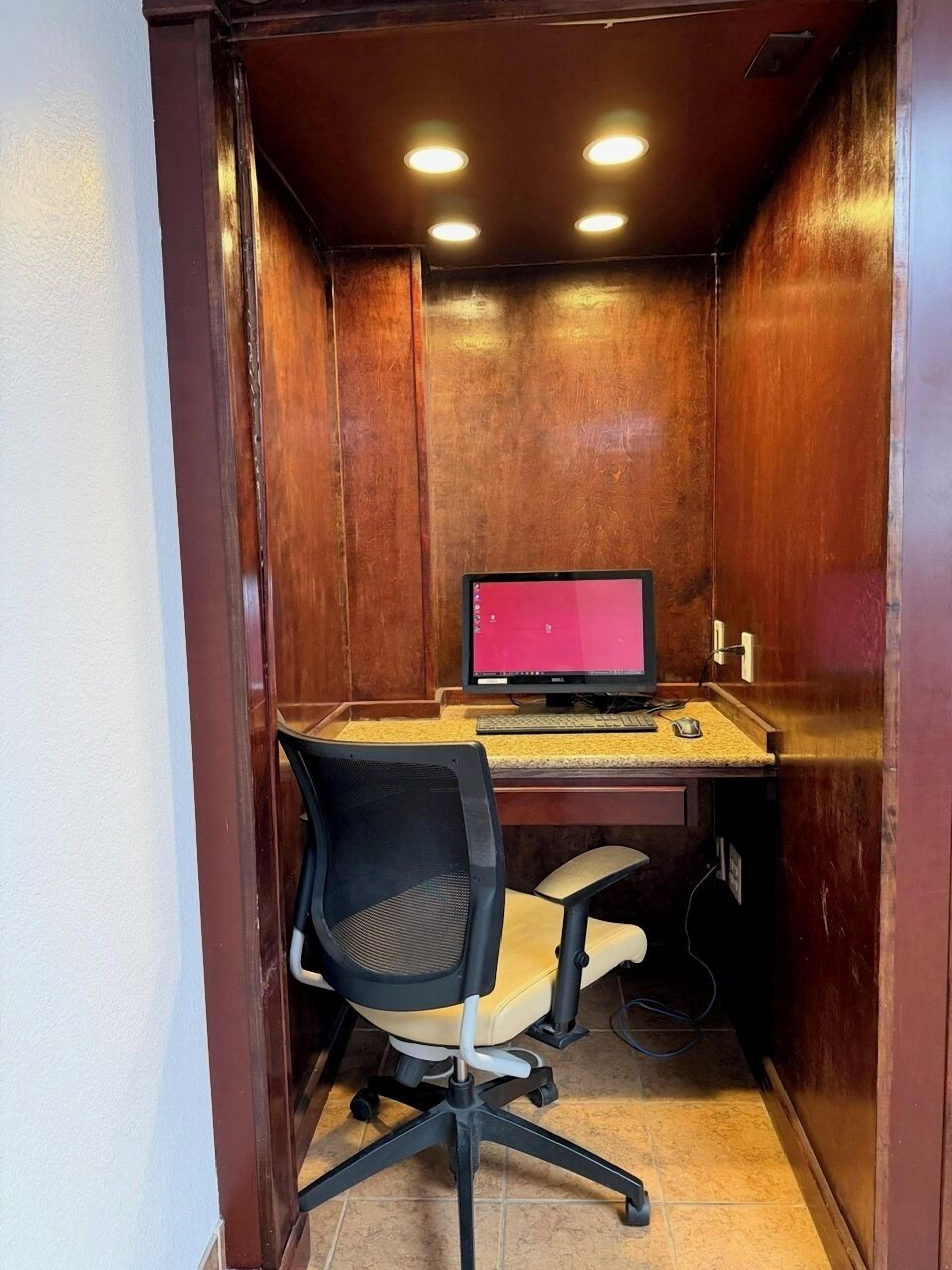 Un petit bureau fermé, comprenant un bureau, une chaise, un ordinateur et deux lampes au plafond.