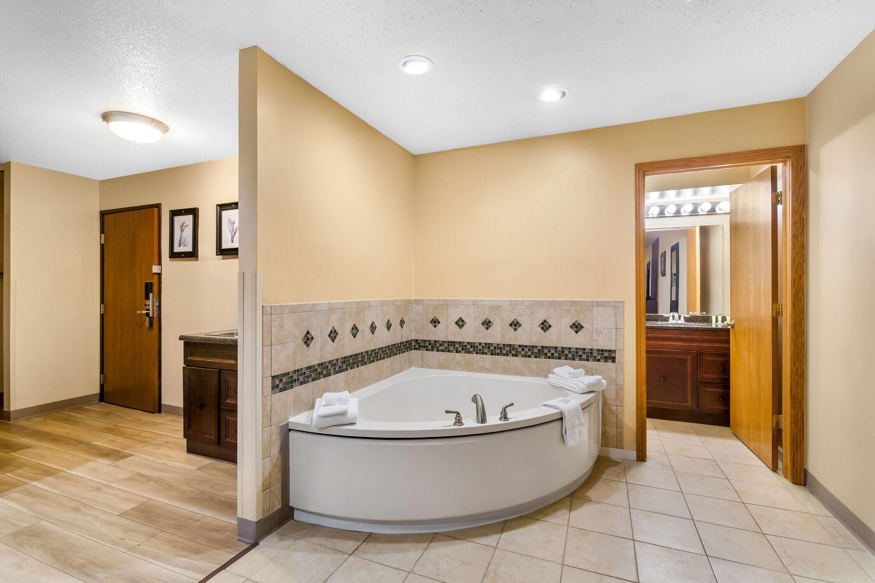 A bathroom with a large bathtub, a wooden door, and a tiled floor.