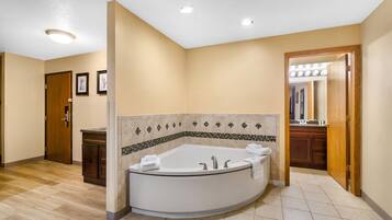 A bathroom with a large bathtub, a wooden door, and a tiled floor.