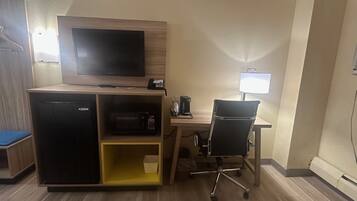 Habitación de hotel con escritorio, silla, televisor, microondas y un pequeño armario.