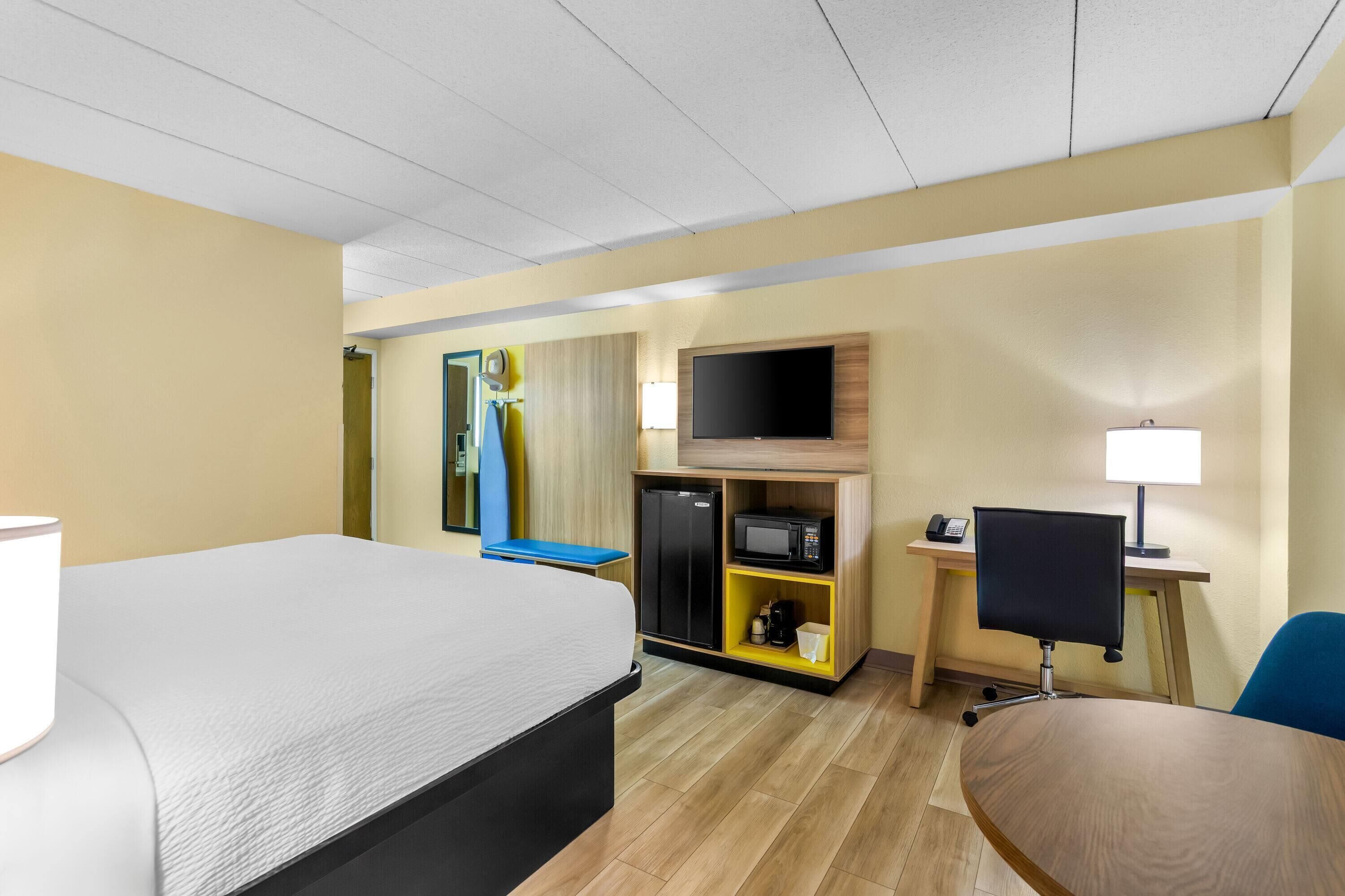 A hotel room with a bed, desk, TV, and a minibar.