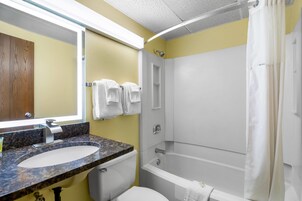 Un baño con lavamanos de granito, inodoro, bañera y cortina de ducha.