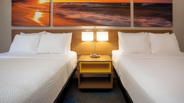 Ein Hotelzimmer mit zwei Betten, einem Nachttisch mit Lampe und drei Sonnenuntergangsbildern an der Wand.