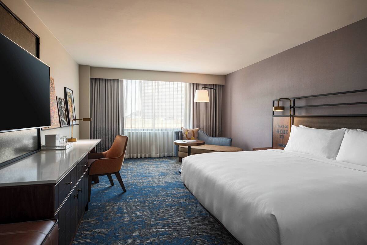 A hotel room with a large bed, a desk with a chair, a small round table, and a TV.