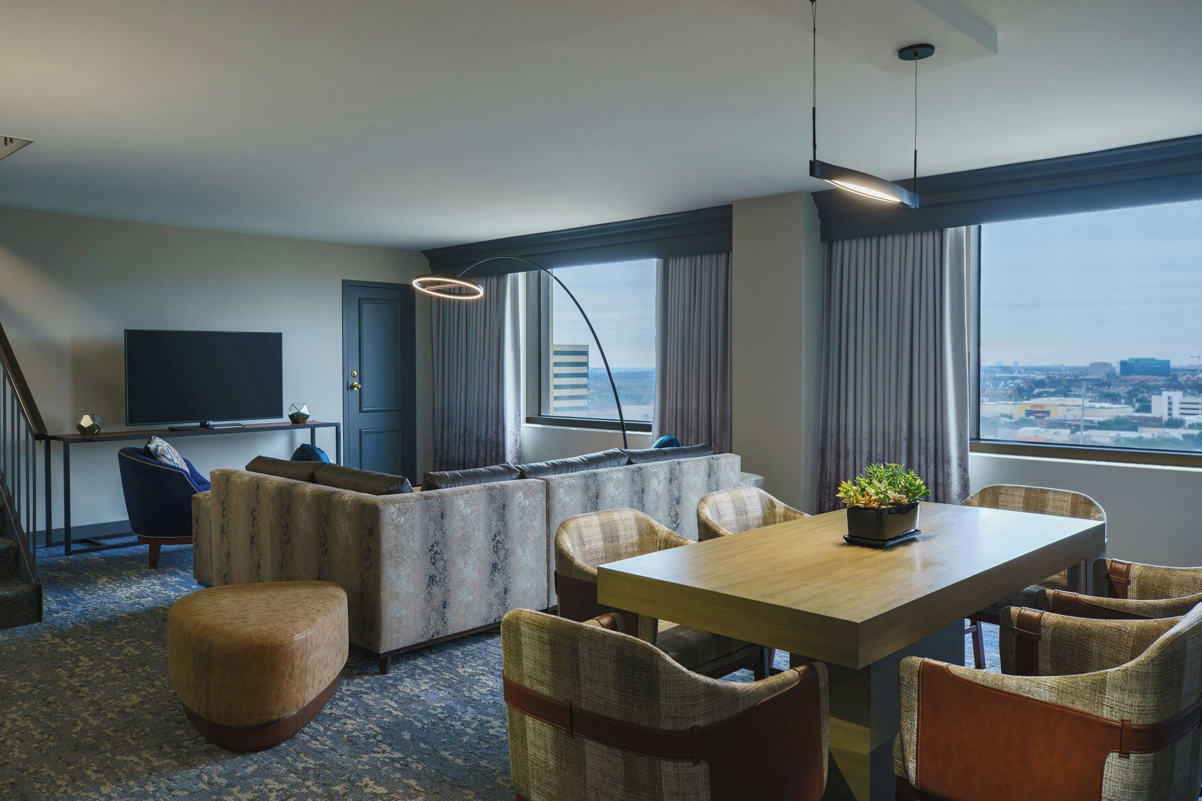 Una habitación de hotel moderna con sofá, mesa de comedor, sillas, televisor y vista a la ciudad.