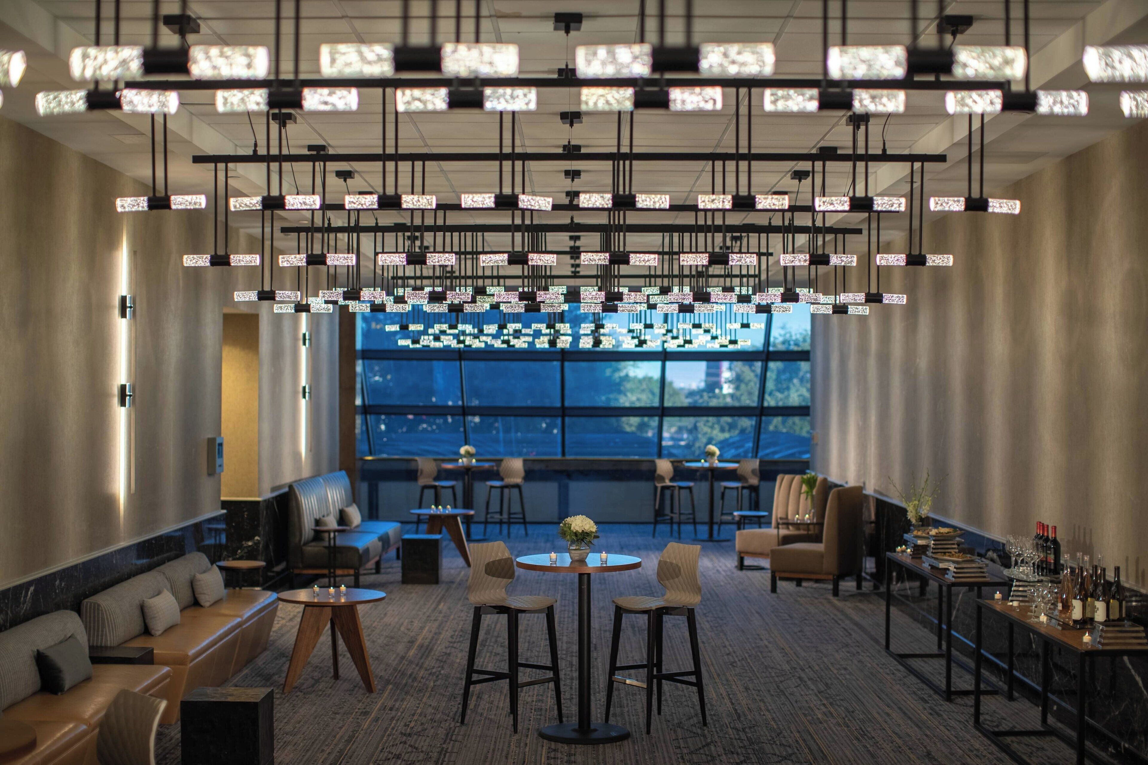 A modern hotel lobby with a seating area, a bar, and a large window offering a view.