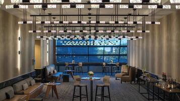 A modern hotel lobby with a seating area, a bar, and a large window offering a view.