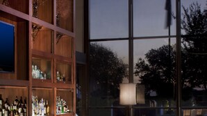 A bar area with a polished marble countertop, wooden shelving with bottles, and upholstered bar chairs. - Renaissance Dallas Addison Hotel (Addison)