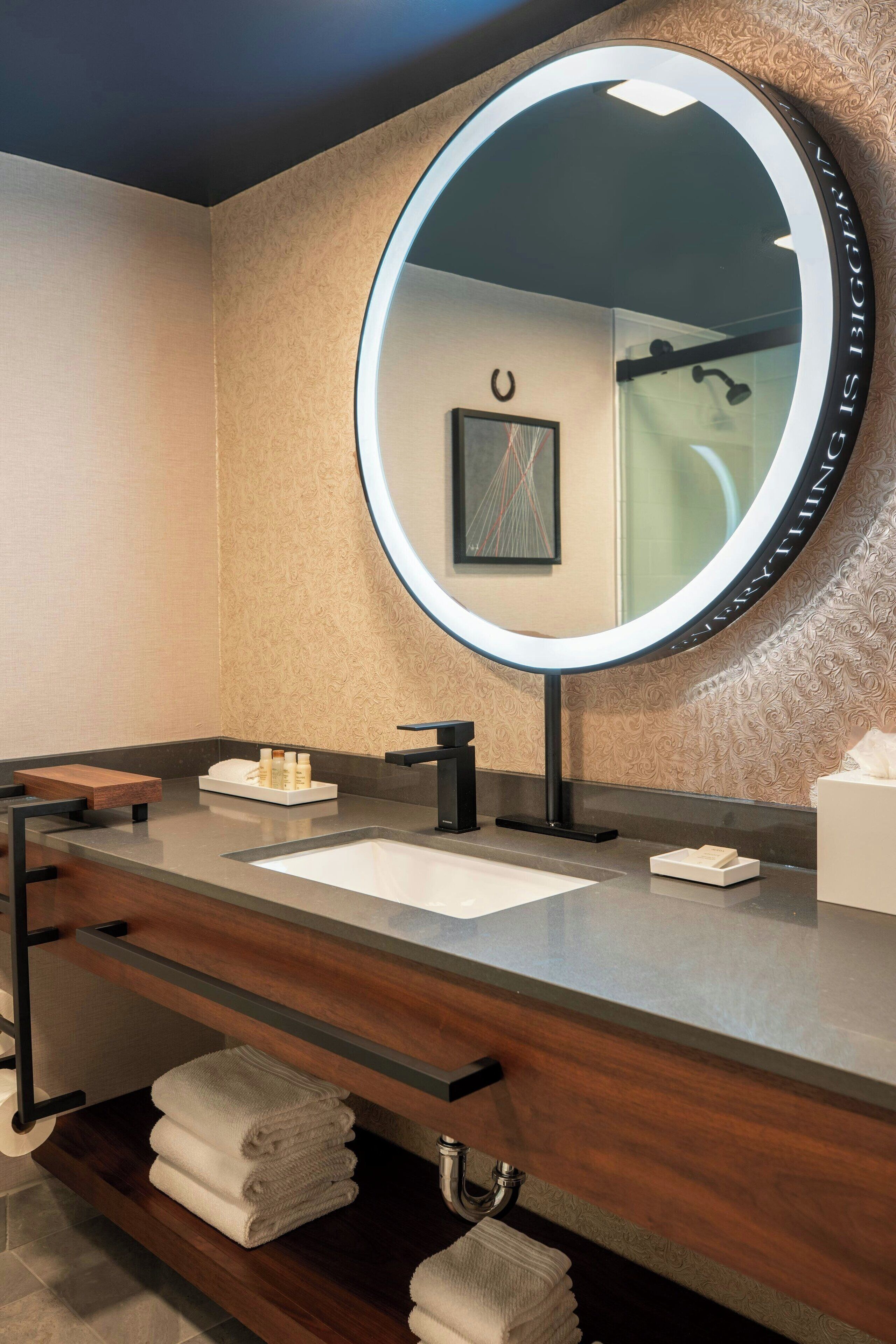 A modern bathroom with a round mirror, wooden vanity, and a towel rack.