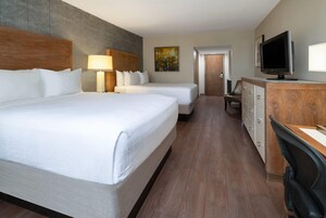 Habitación de hotel con dos camas, un escritorio con televisor, cómoda y un cuadro en la pared.