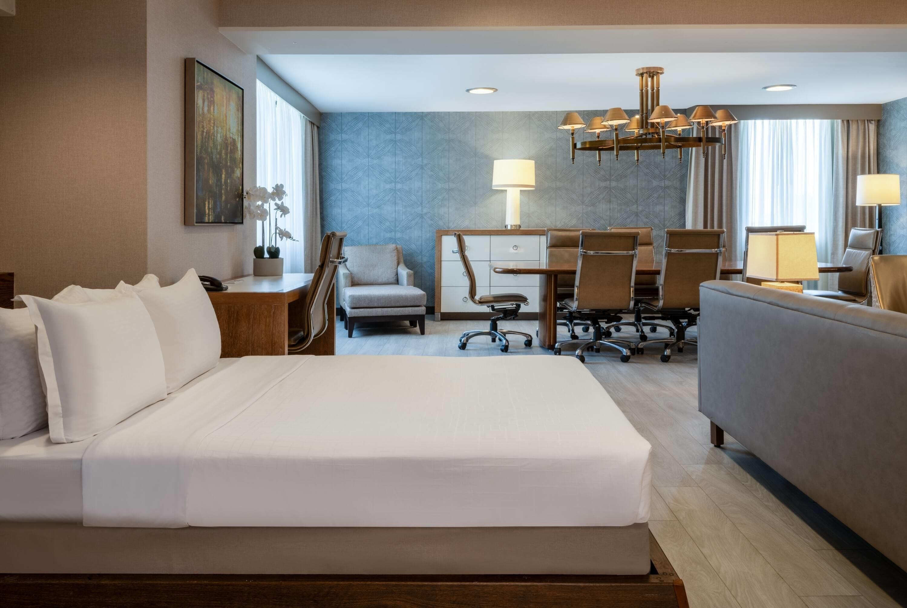 A hotel room with a large bed, a sofa, a desk with chairs, and a dining table.